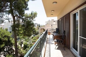 A balcony with a table and chairs, overlooking a garden and buildings. - Spacious 4BR Glyfada Retreat Near the Coast (Glifada)
