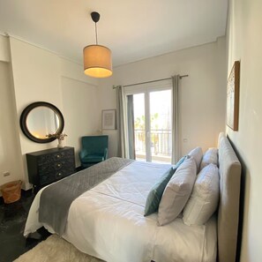 A bedroom with a bed, a dresser, a chair, a hanging light fixture, and a view of the outdoors through a window. - Spacious 4BR Glyfada Retreat Near the Coast (Glifada)