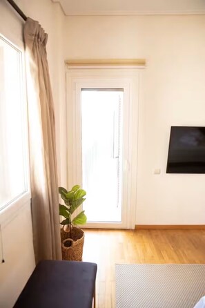 A room with a sliding door, a potted plant, a flat-screen TV, and a small table. - Spacious 4BR Glyfada Retreat Near the Coast (Glifada)