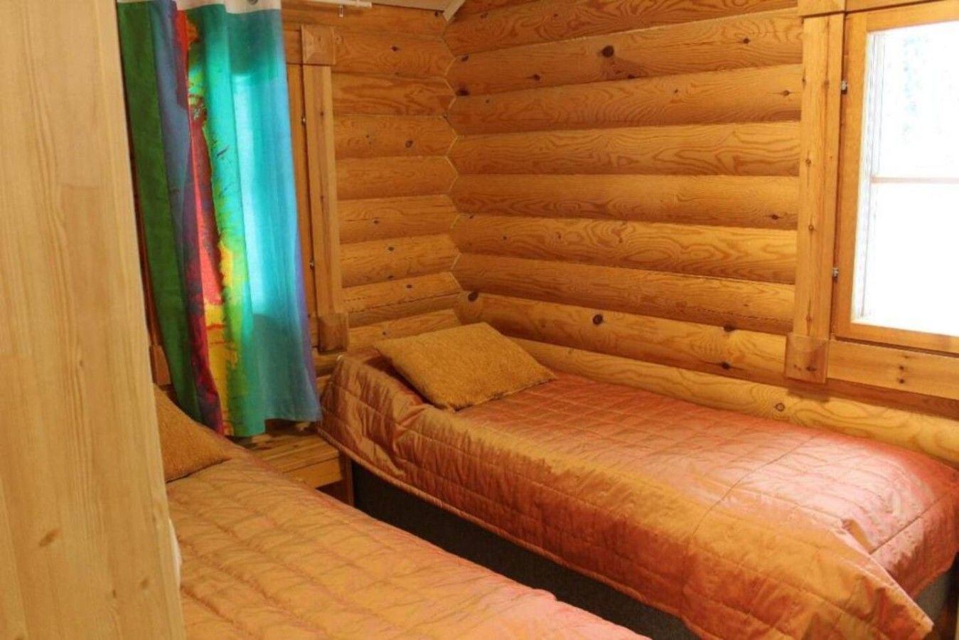 A cabin with a wooden interior, a bed with a quilt, and a window with curtains.