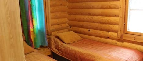 A cabin with a wooden interior, a bed with a quilt, and a window with curtains.