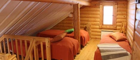 Ein Schlafzimmer in einer Blockhütte mit zwei Betten, einem Fenster und einer Holzbalkendecke.