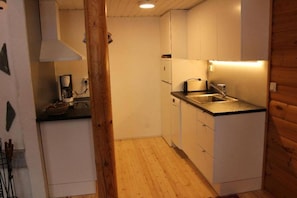 A compact kitchen with white cabinets, a black countertop, and a wooden floor. - Honkaruka | Homelike 1BR Apt with Private Sauna (Ruka)