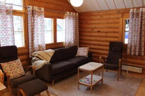 A log cabin interior with a sofa, armchairs, a small table, and patterned curtains. - Honkaruka | Homelike 1BR Apt with Private Sauna (Ruka)
