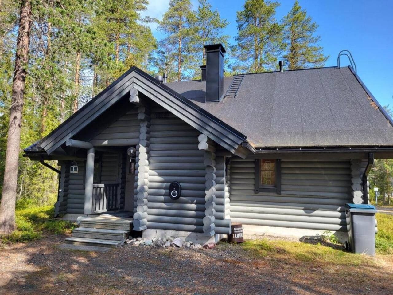 A log cabin with a front porch, a chimney, and a small attached shed.