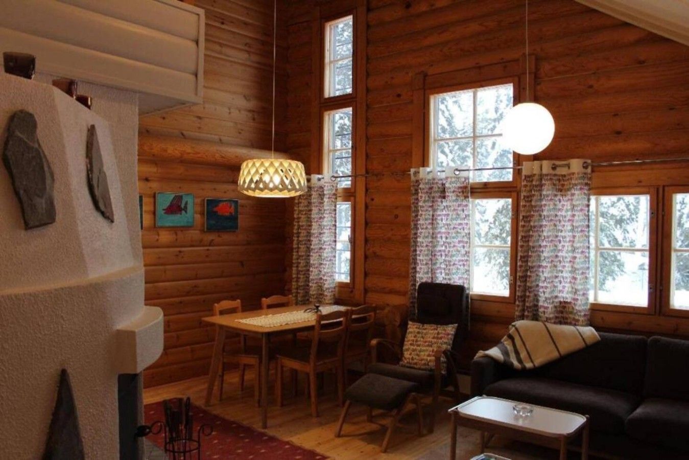 A log cabin interior with a dining area, a sofa, and a hanging light fixture.