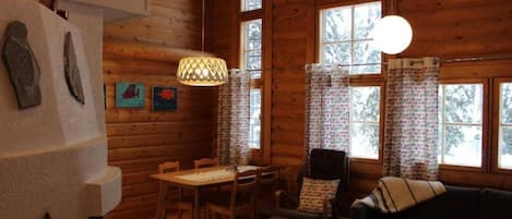 A log cabin interior with a dining area, a sofa, and a hanging light fixture.