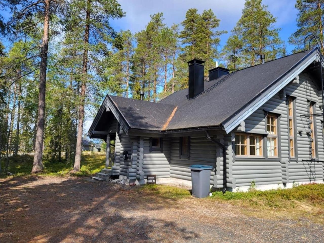 En hytte med skorsten, veranda og skraldespand.