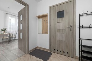 Een kamer met een houten deur, een spiegel, een kapstok en een zithoek met een tafel en stoelen.