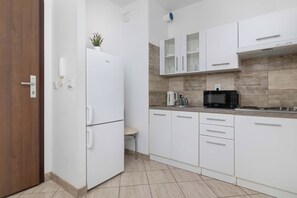 A modern kitchen with white cabinetry, a built-in microwave, and a coffee machine. - A Practical Studio Flat with a Balcony | Close to the City Centre (Kraków)