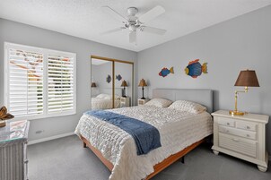 A bedroom with a bed, bedside tables, a ceiling fan, a window with blinds, and wall decorations.