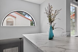 A bathroom with a marble countertop, a vase with flowers, a window with a view of a building, and a ceiling light.