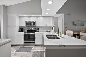 A modern kitchen with white cabinetry, stainless steel appliances, a marble countertop, and a built-in oven.