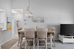 Un comedor moderno con una mesa y sillas, una lámpara colgante y un televisor de pantalla plana sobre un soporte.