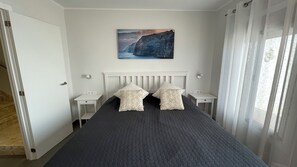 A bedroom with a bed, two bedside tables, a nightstand, a painting on the wall, and a window with curtains. - Pleasant 2-bedroom apartment with AC in charming CN (CN)