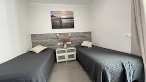 Une chambre d’hôtel avec deux lits simples, une table de chevet avec un vase et un tableau représentant une scène de plage.