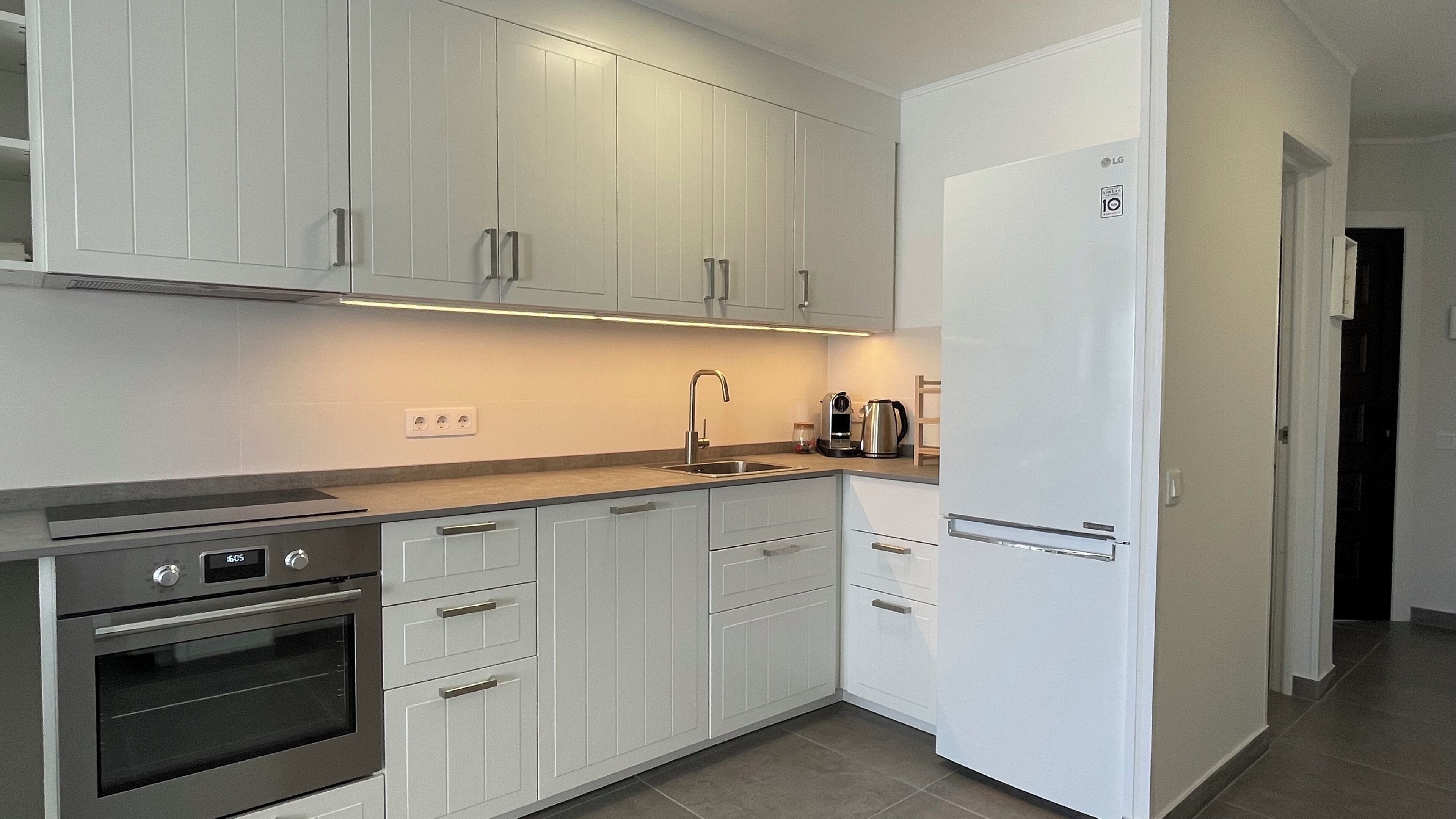 A modern kitchen with white cabinets, a stainless steel oven, a built-in dishwasher, and a white refrigerator.