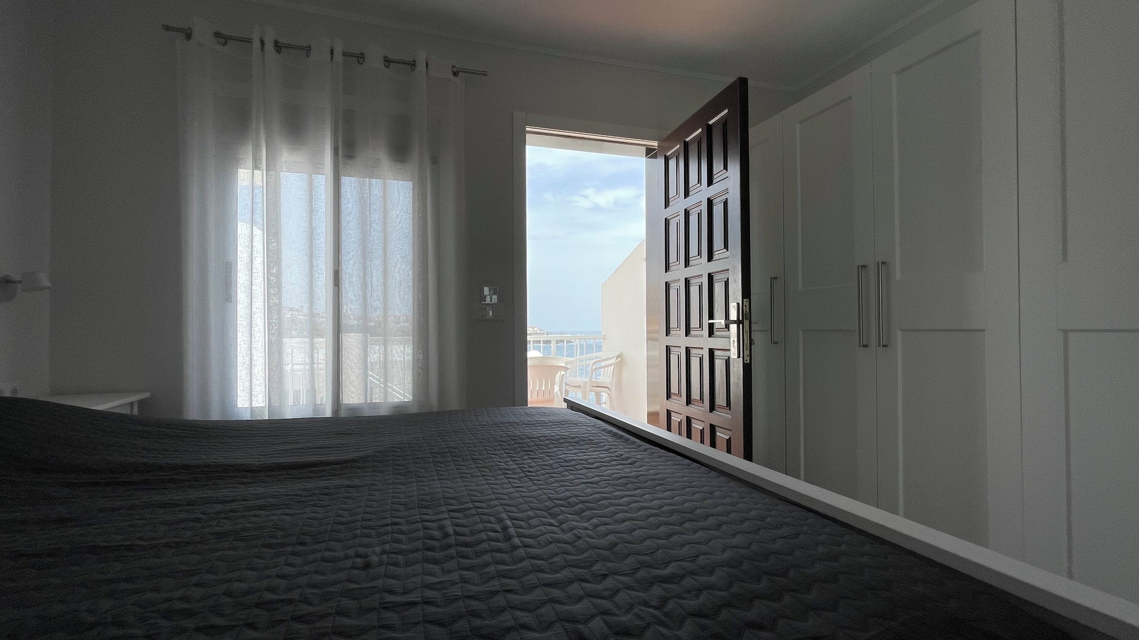 A bedroom with a bed, a wardrobe, and a view of the outside.