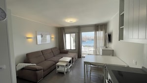 Un soggiorno moderno con un divano, un tavolino, una televisione e un balcone vista mare.