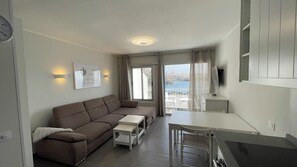 A modern living room with a sofa, a small table, a TV, and a balcony with a view of the sea. - Pleasant 2-bedroom apartment with AC in charming CN (CN)