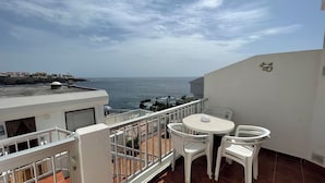 Un balcone con tavolo e sedie, affacciato su una vista costiera con rocce e mare.