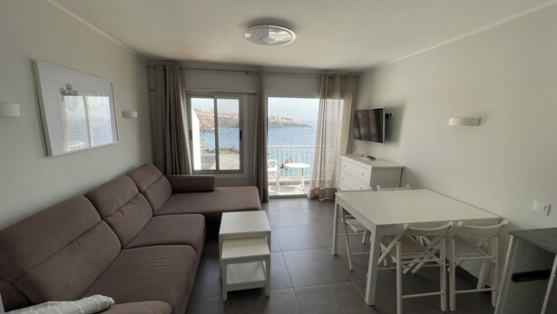 Una moderna camera d'albergo con divano, un tavolino, una TV e un balcone vista mare.
