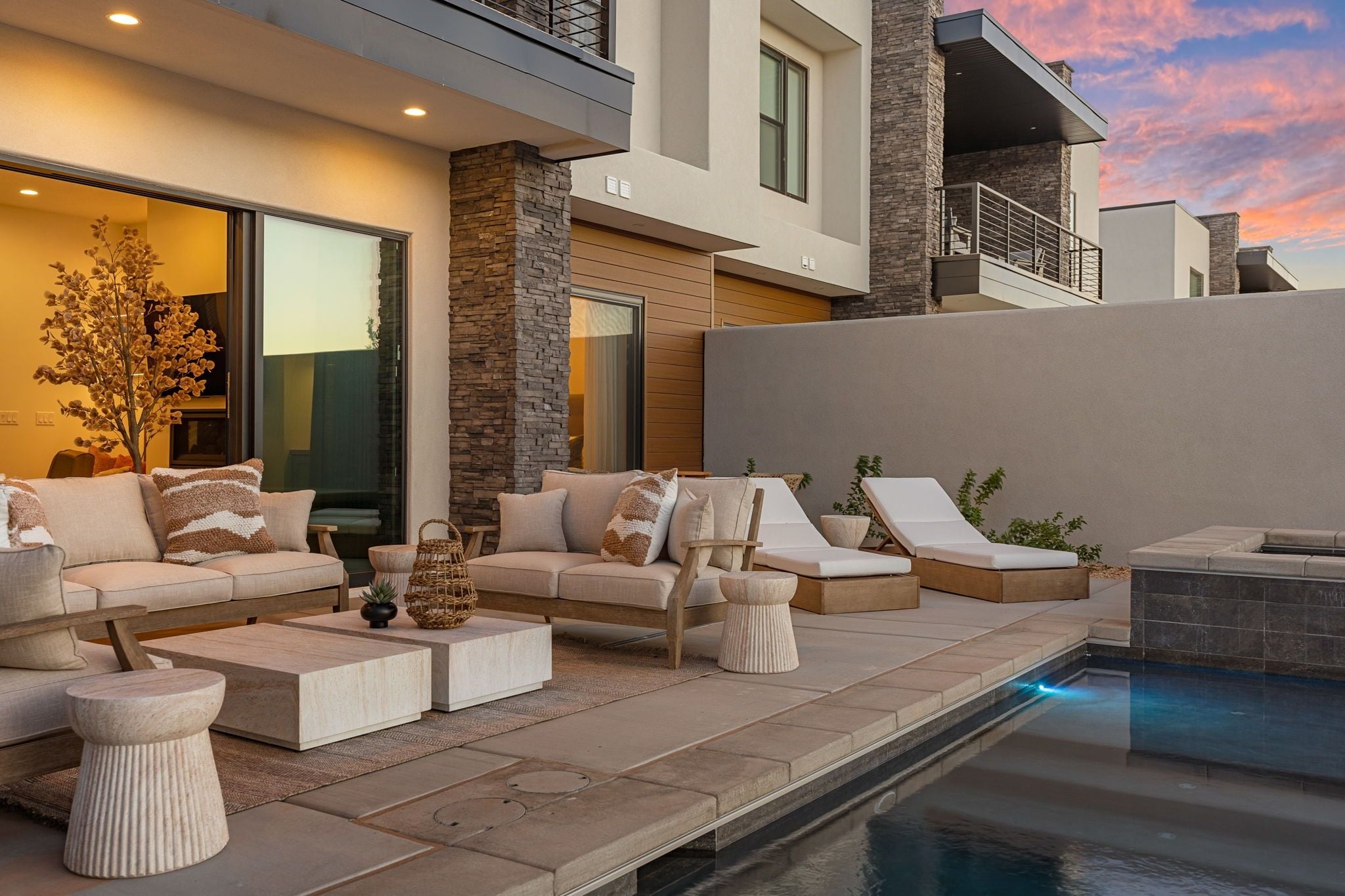 Et moderne udendørs opholdsområde med pool, inklusive en sofasæt, liggestole og et lille bord.