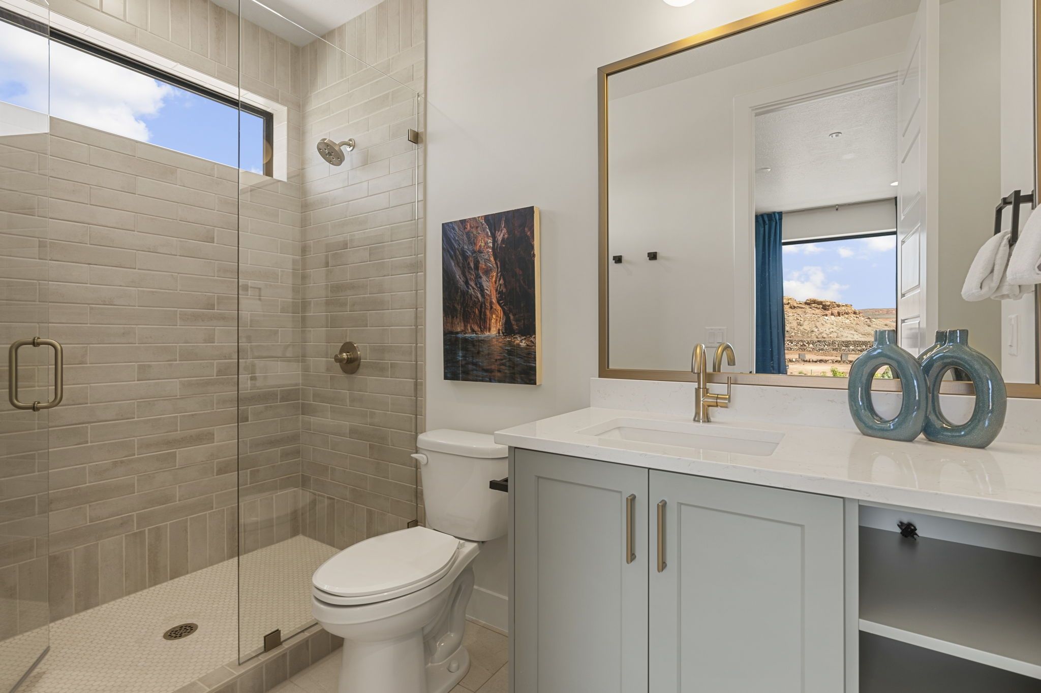 Un baño moderno con ducha de vidrio, inodoro, lavamanos con grifo dorado y un espejo grande.