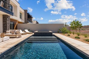 Uma área de piscina moderna ao ar livre, com espreguiçadeiras e um muro de pedra.