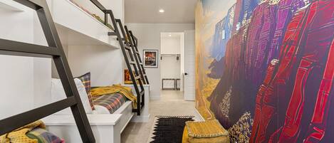 A modern interior with a staircase, a large mural, and a bed with colorful bedding.