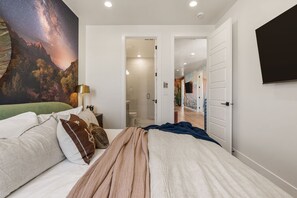 A bedroom with a bed, pillows, a nightstand, a lamp, and a wall mural. - Red Rock Isle 7 Bedroom Townhouse (Washington)