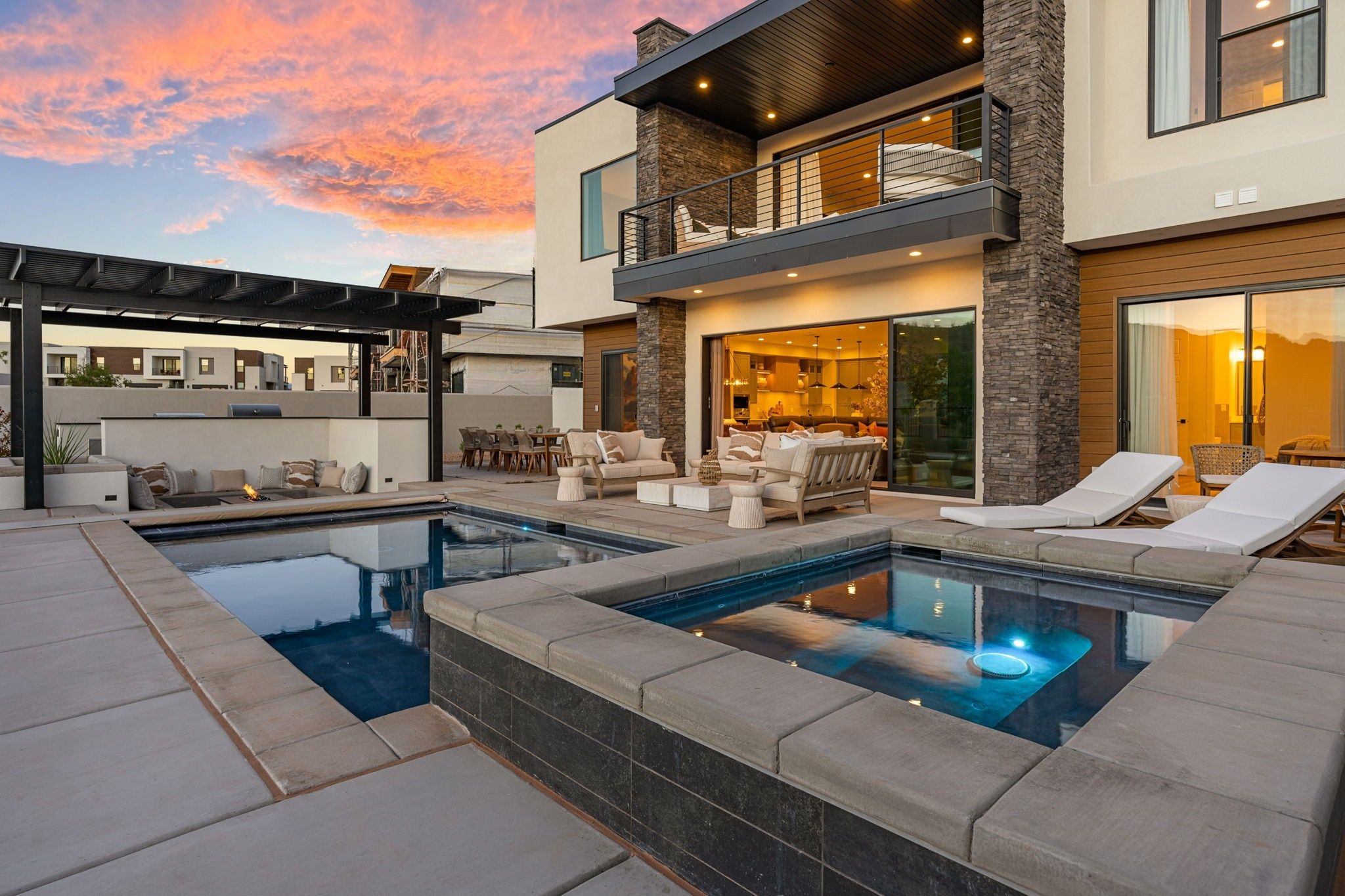 Une maison moderne à deux étages dotée d’une terrasse sur le toit, d’une piscine et d’un patio aménagé avec du mobilier d’extérieur.