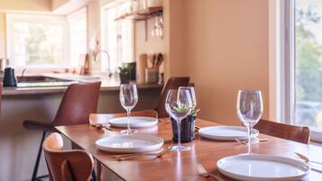 A dining table set with plates, glasses, and cutlery, with a view of the kitchen in the background.