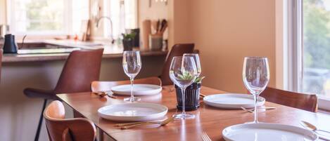 A dining table set with plates, glasses, and cutlery, with a view of the kitchen in the background.