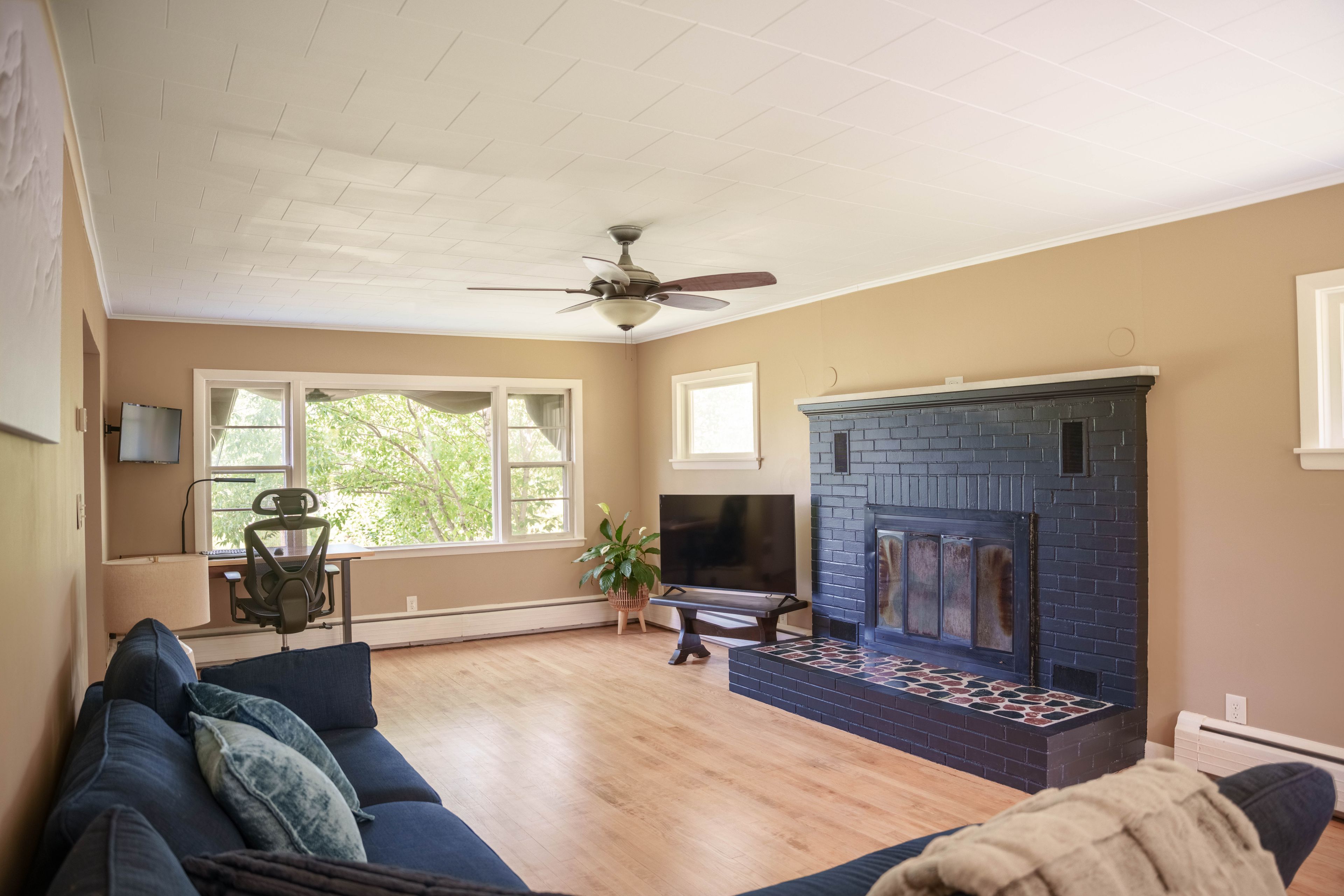 Una sala de estar con chimenea, ventilador de techo y un ventanal grande.