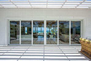 Eine moderne Villa mit großen Schiebeglastüren, die zu einem Poolbereich mit Meerblick führen.