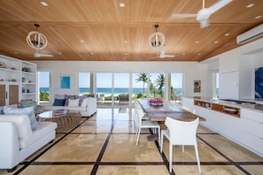 A modern kitchen with a wooden ceiling, white cabinetry, and a view of the ocean. - Coralli - Contemporary Beachfront Escape With Private Pool 3 Bedroom Home (Savannah Sound)