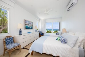 A bedroom with a large bed, a dresser, a chair, and a view of the ocean. - Coralli - Contemporary Beachfront Escape With Private Pool 3 Bedroom Home (Savannah Sound)