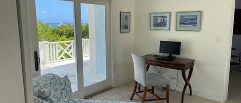 A room with a sliding glass door leading to a balcony, a desk with a computer, and two framed pictures on the wall.