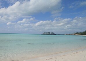 A beach with clear turquoise water, a sandy shore, and a small island with trees in the distance.