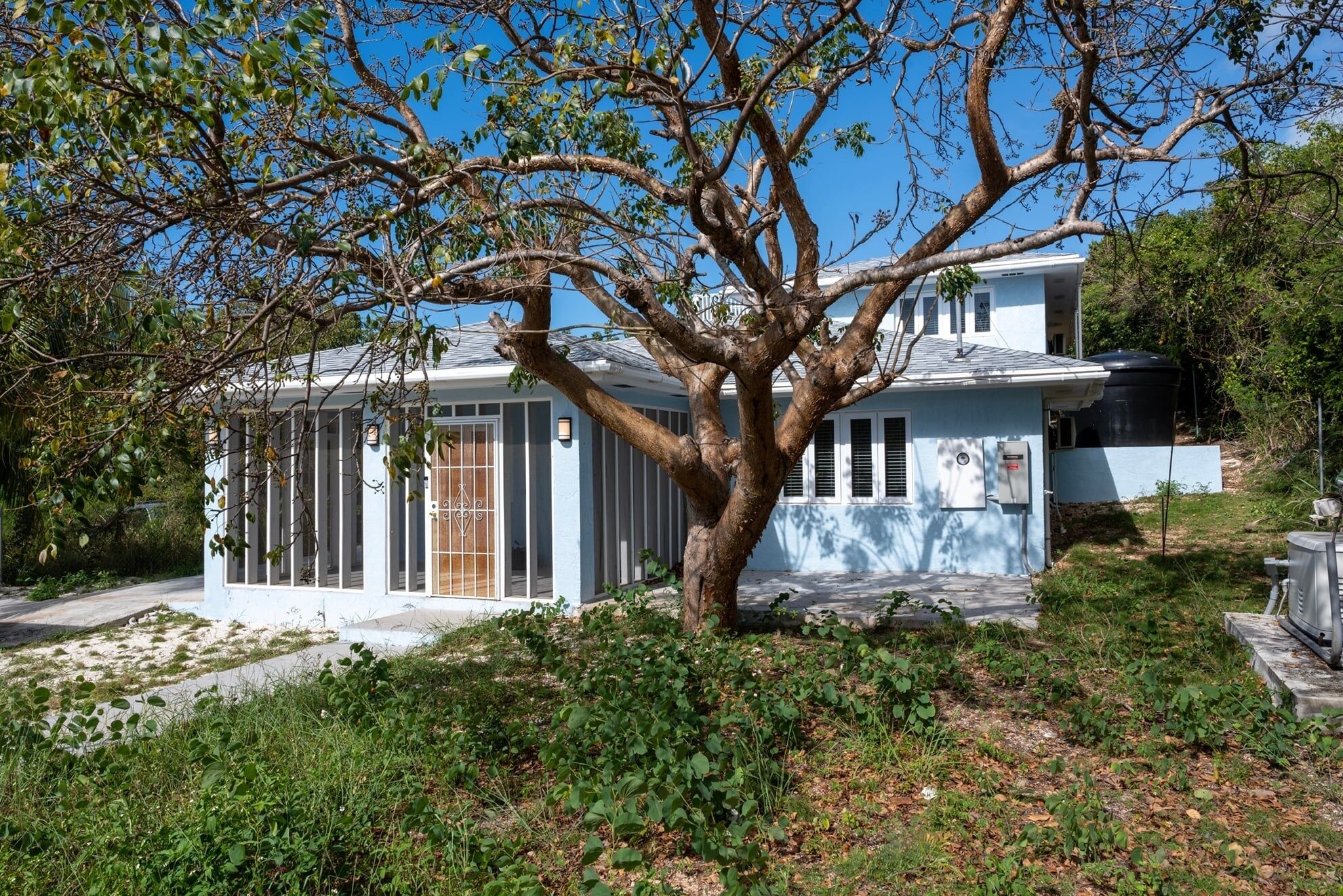 A house with a large tree in front, a garage, and a small porch area.