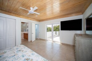 A spacious bedroom with a wooden ceiling, a ceiling fan, a bed with a floral bedspread, a built-in wardrobe, and a sliding glass door leading to a balcony.