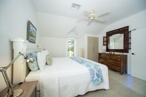 Quarto com cama, luminária de cabeceira, penteadeira, espelho e ventilador de teto.