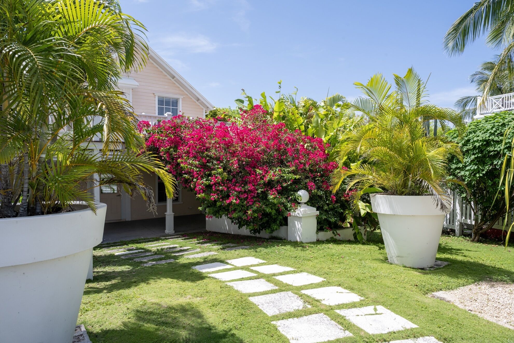 A well-maintained garden with a paved pathway, lush greenery, and a variety of flowering plants.