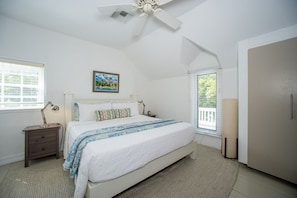 A bedroom with a bed, bedside tables, a ceiling fan, a window with blinds, and a door. - Peach House Up - Stylish And Sunny Top Floor Suite Walk To Town 1 Bedroom Apts (Governor's Harbour)
