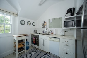 A compact kitchen with white cabinets, a built-in oven, a dishwasher, a microwave, and a coffee maker. - Peach House Up - Stylish And Sunny Top Floor Suite Walk To Town 1 Bedroom Apts (Governor's Harbour)