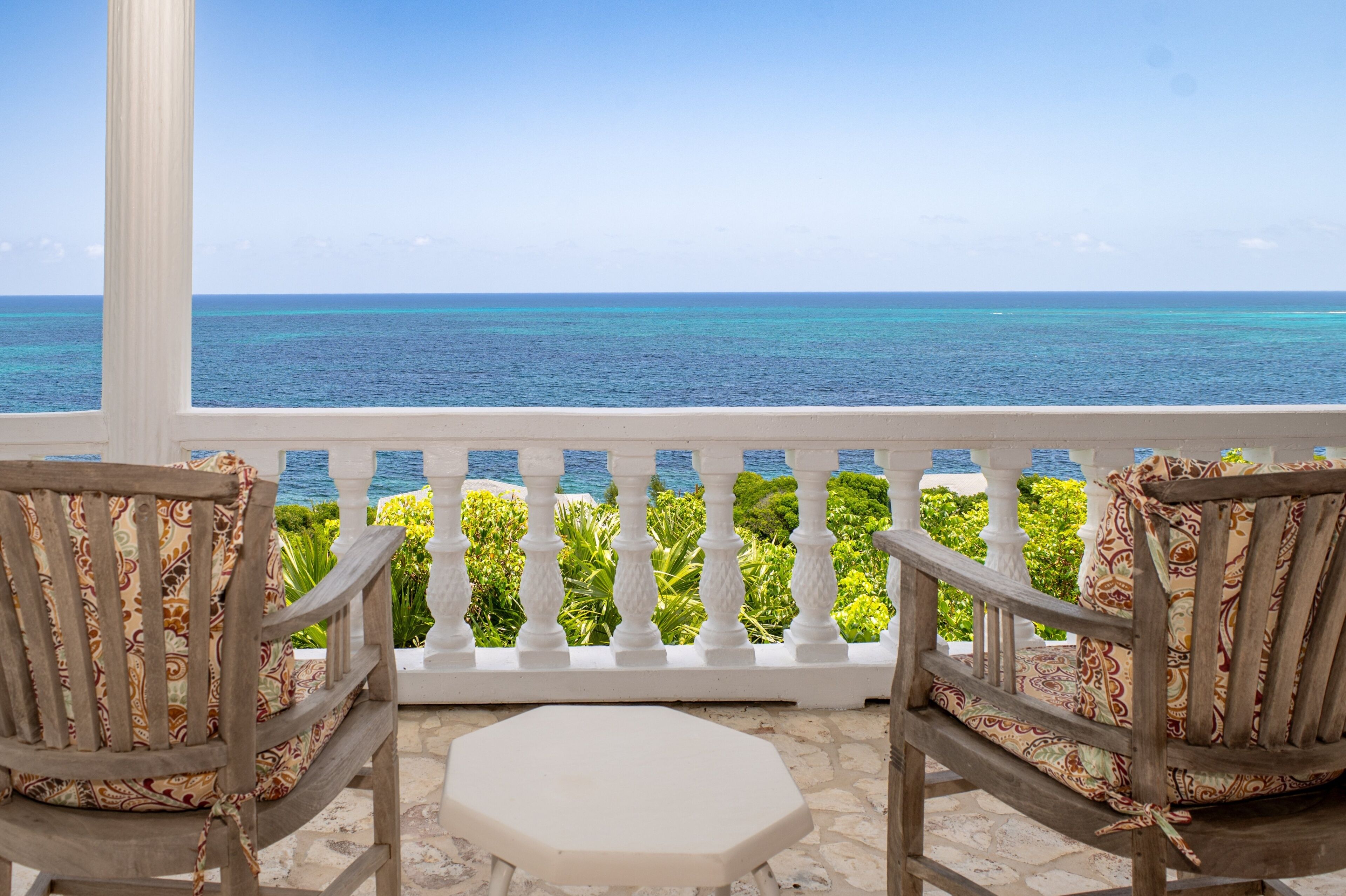 A balcony with two wooden chairs and a small table, overlooking a turquoise sea.
