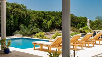 A pool area with lounge chairs, a clear blue pool, and a backdrop of dense greenery.