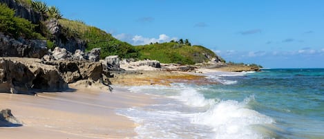 Una playa con aguas cristalinas, acantilados rocosos y vegetación.