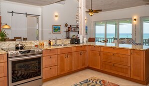 A kitchen with a large island, stainless steel appliances, wooden cabinets, and a view to the outside. - High Life - Private Hilltop Estate With Pool And Panoramic Ocean 4 Bedroom Home (Governor's Harbour)